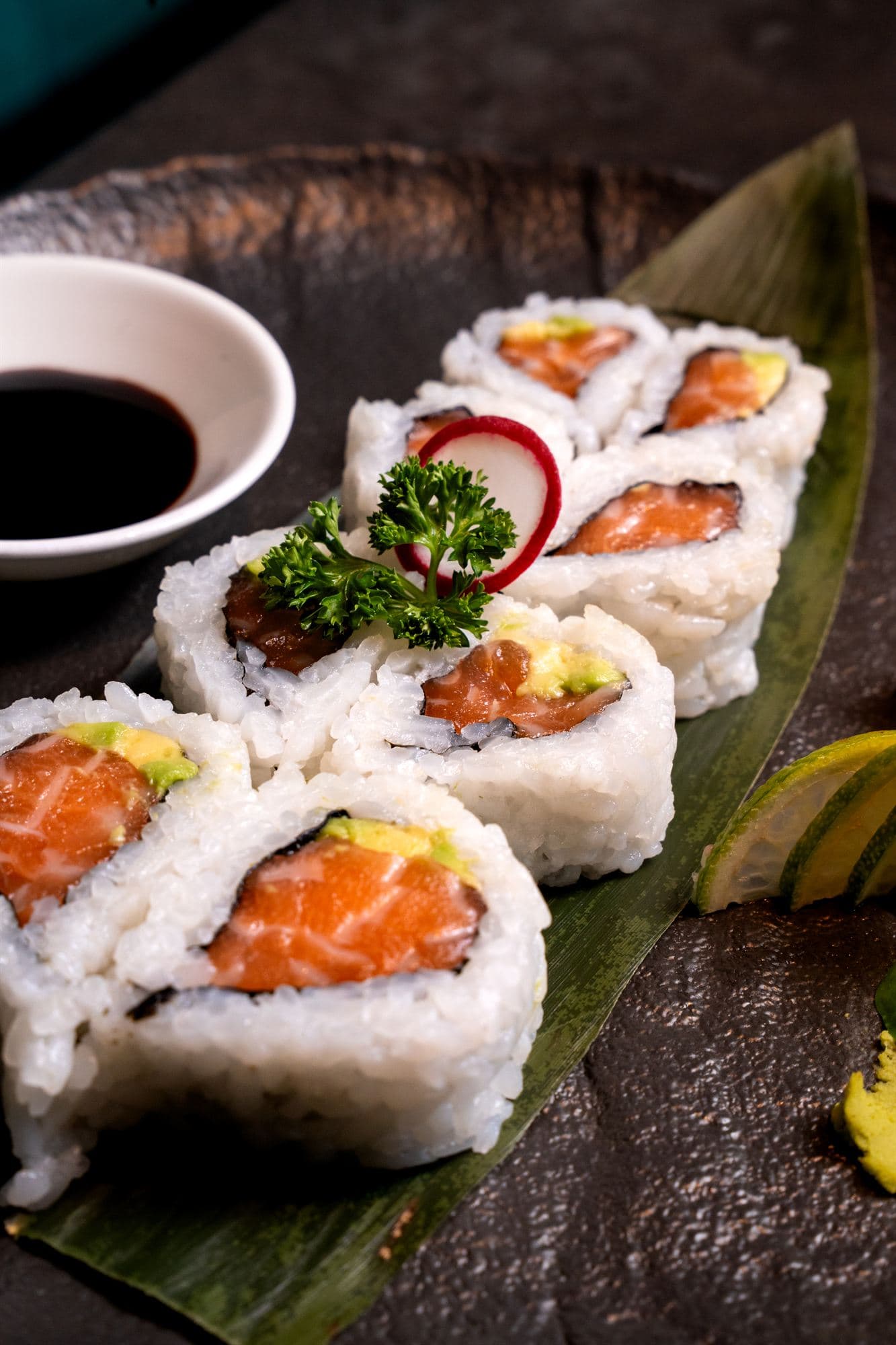 Uramaki di salmone e avocado serviti su foglia con salsa di soia