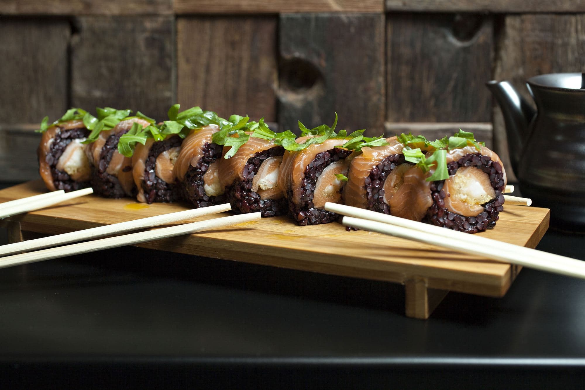 Uramaki di riso venere e rucola serviti su tagliere di legno
