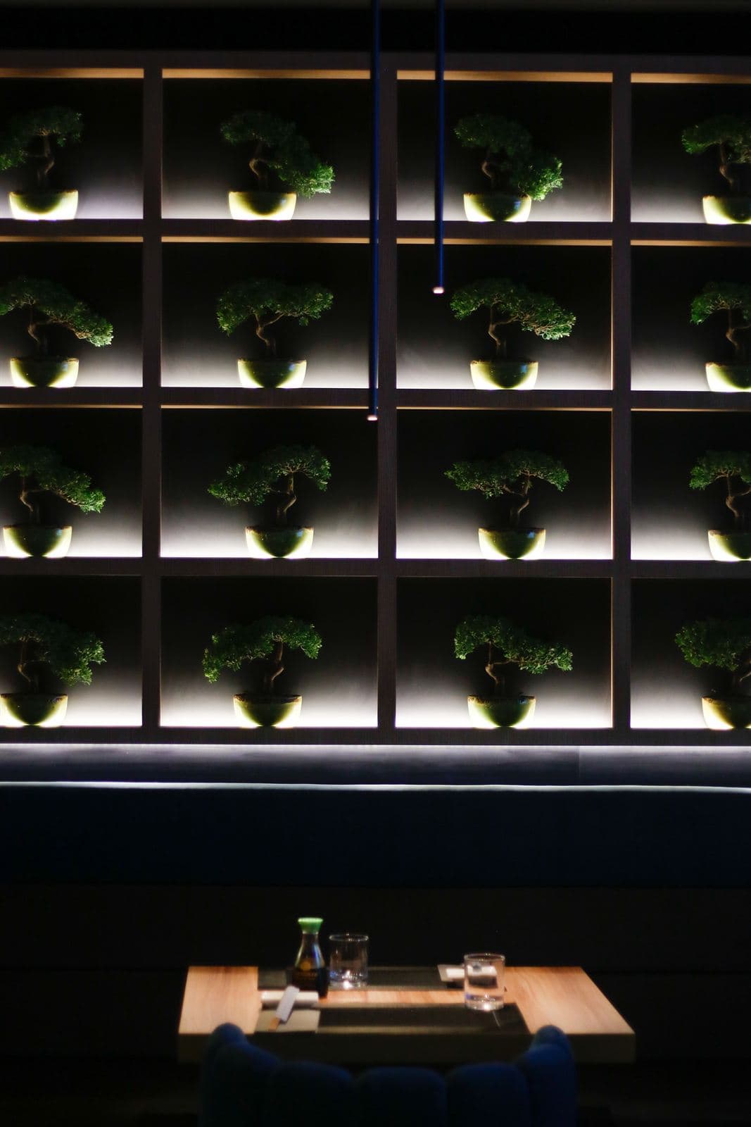 La parete a rombi retroilluminata con i bonsai sopra un tavolo